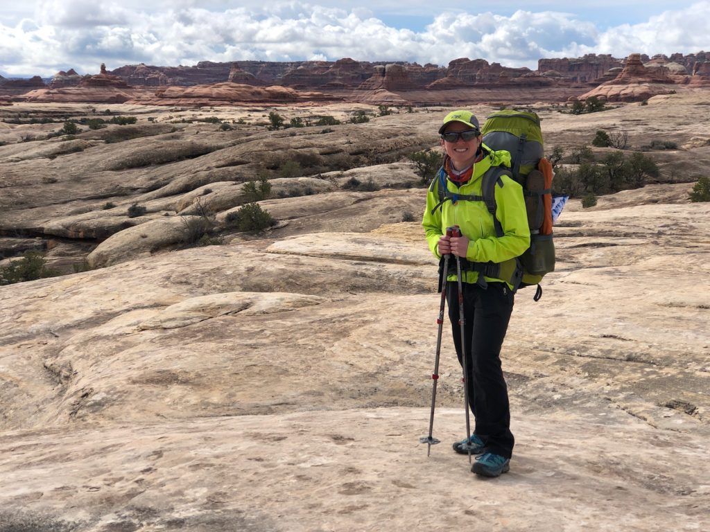 A woman wearing a large backpack stands on a white rock layer in Canyonlands National Park